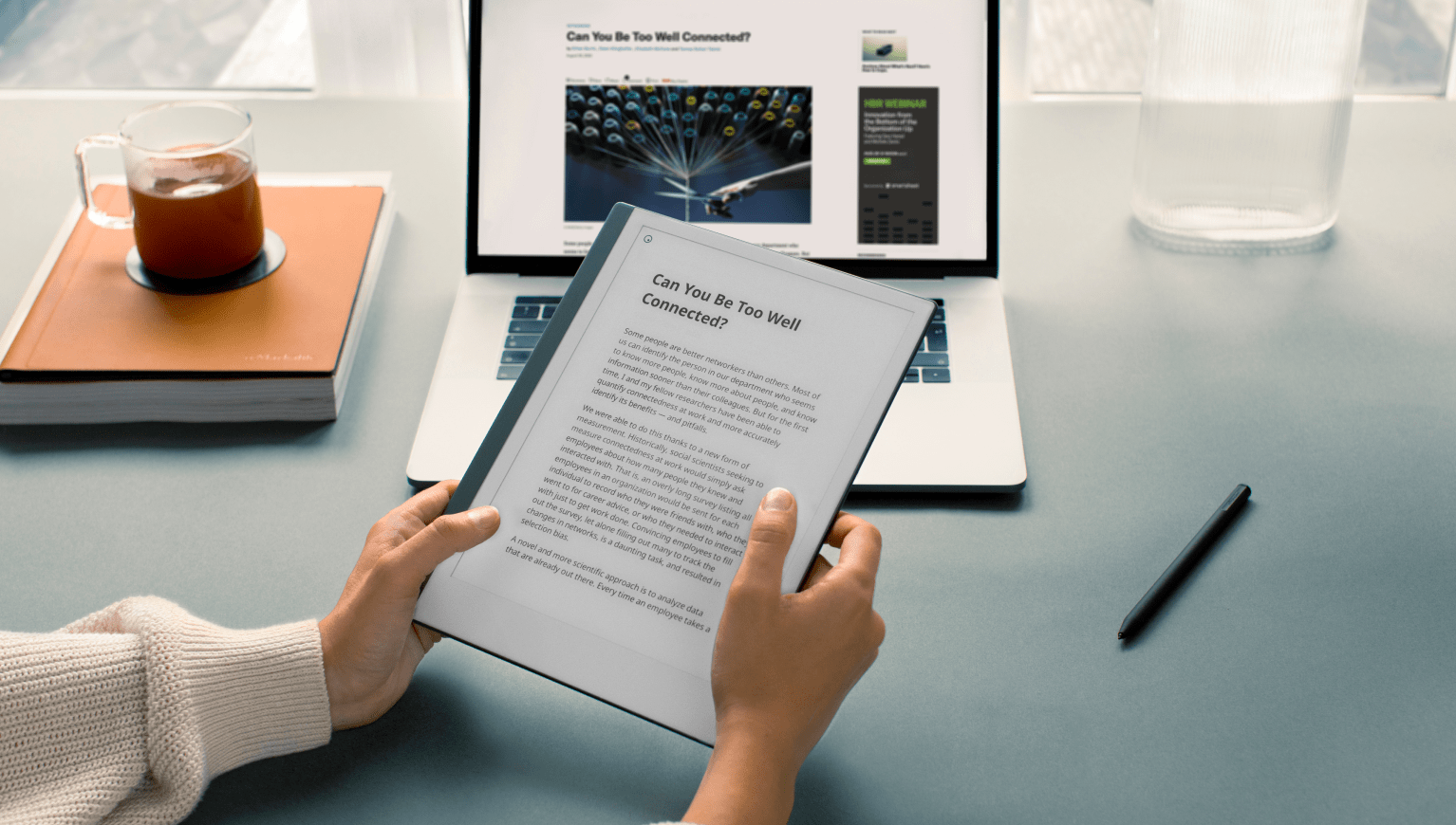 Desk environment showing laptop and hands holding reMarkable paper tablet.