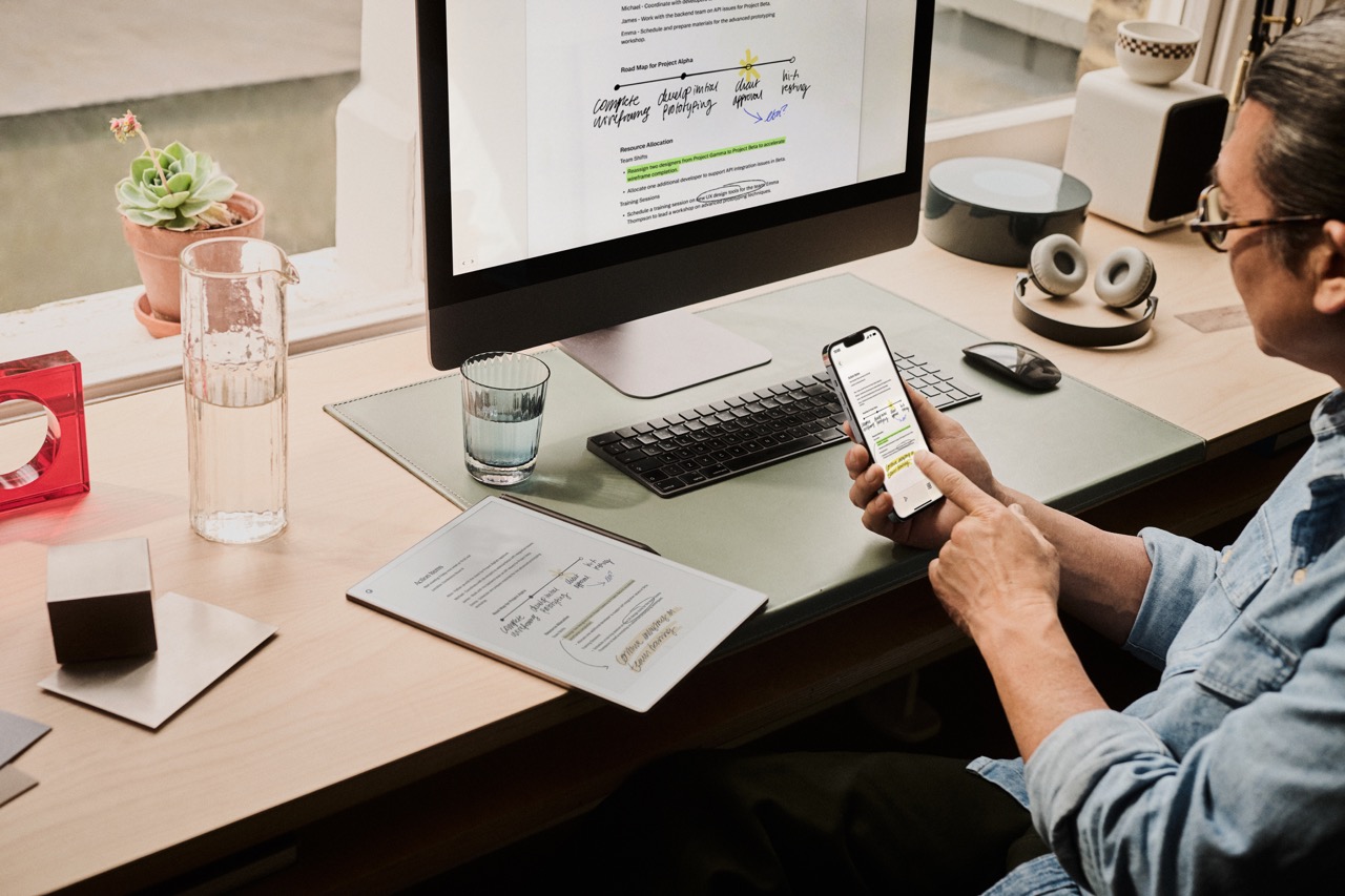 Person sitting by a desk with reMarkable apps on phone and computer display.